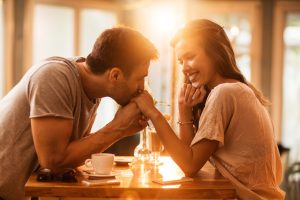 Smiling woman enjoying in a cafe while being kissed in a hand by her boyfriend.